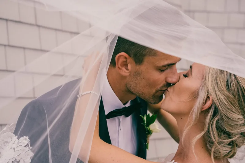 Newlyweds kissing beneath a flowing veil